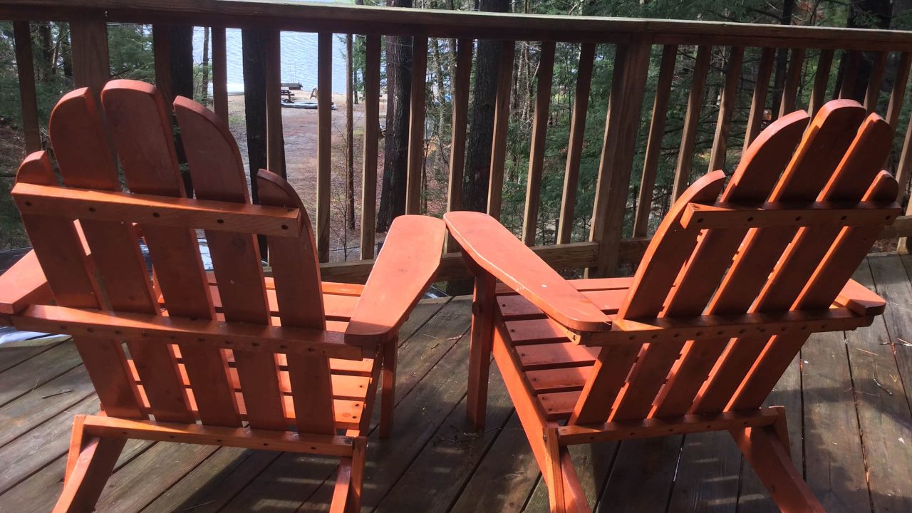 Two Adirondack chairs on the deck with the lake beyond